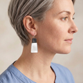 Model with short silver-grey hair wearing charcoal and white earrings
